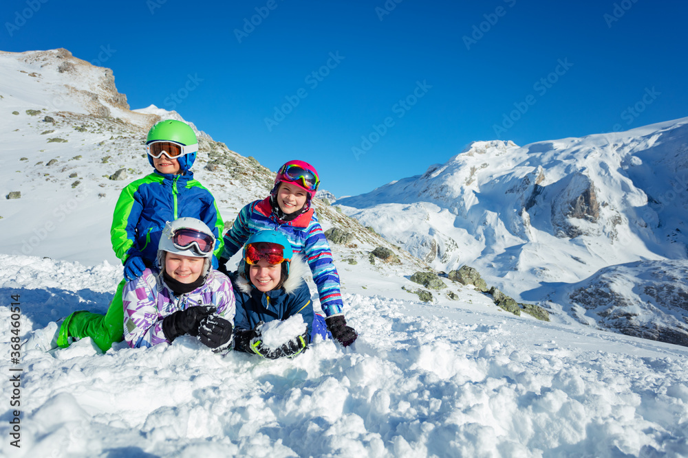 四个微笑快乐的孩子一组穿着滑雪服躺在山顶的雪地里，颜色为hel