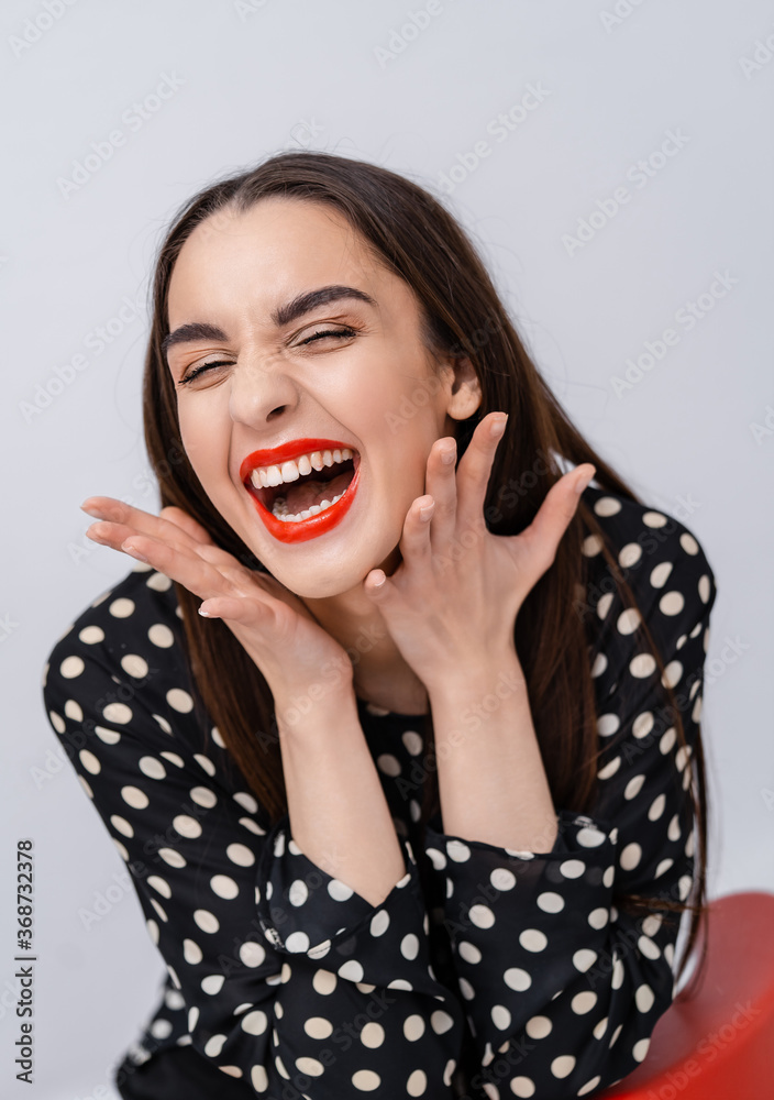 Young beauty with perfect smile, red lips and white teeth. Girl holding finger near red lips. White 