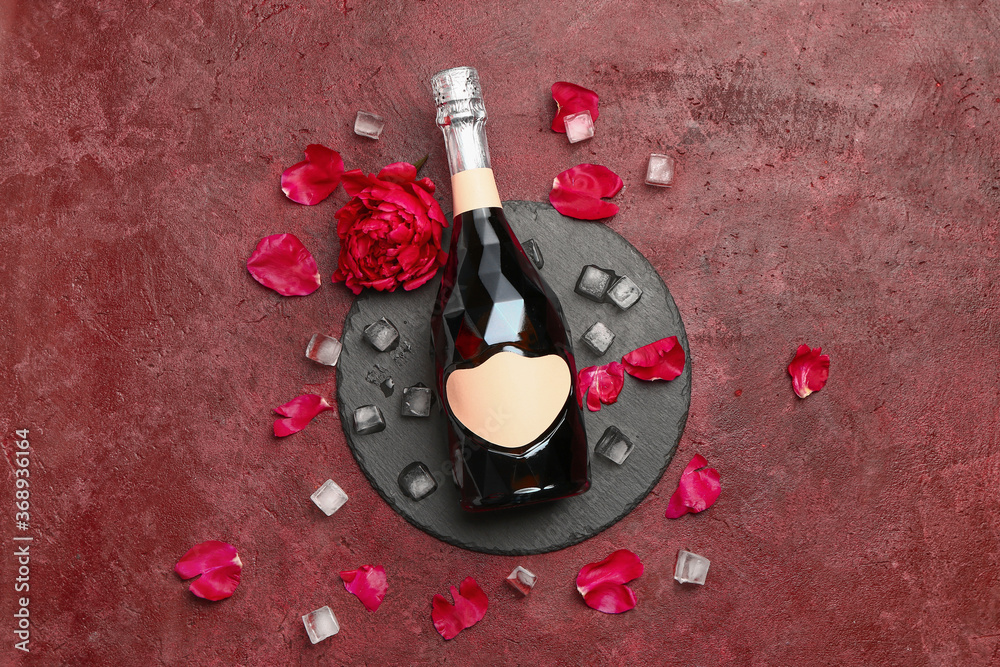 Bottle of champagne, ice cubes and flowers on color background