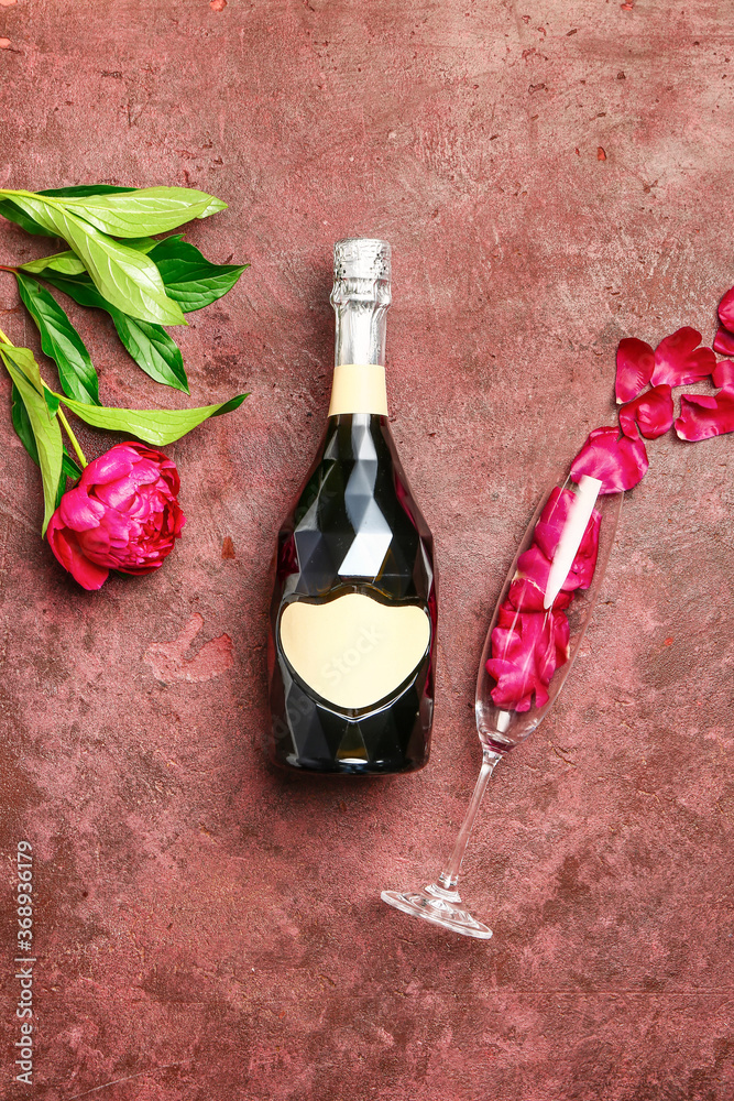 Bottle of champagne, glass and flowers on color background