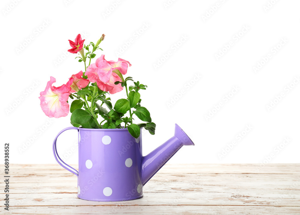 Watering can with flowers on table against white background