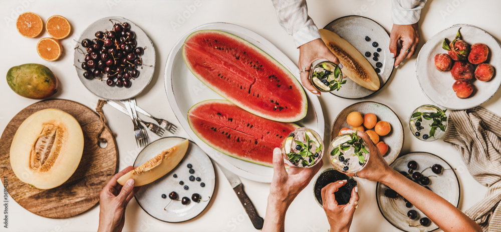 Summer tropical fruit party table. Flat-lay of peoples hands with glasses og lemonade over table wit