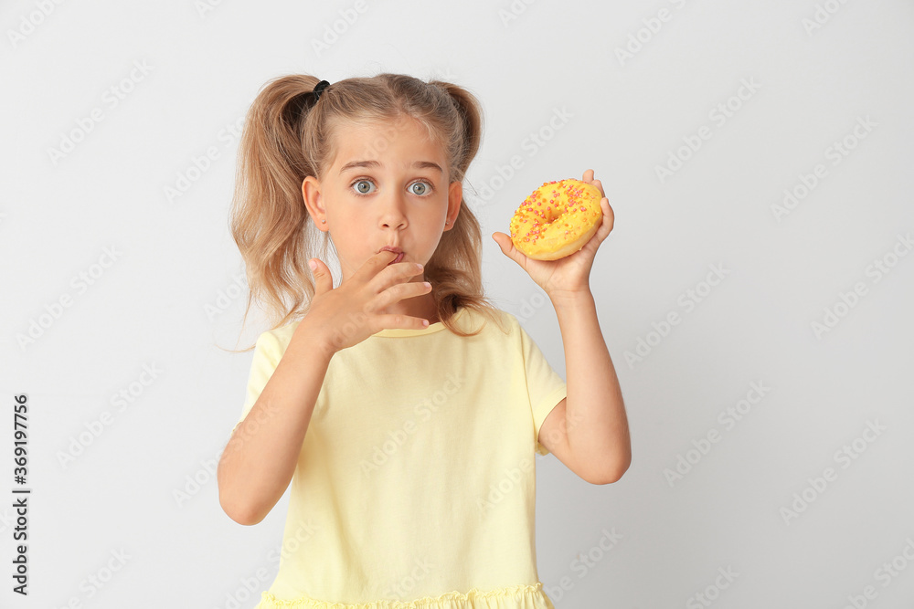 Funny little girl with donut on light background