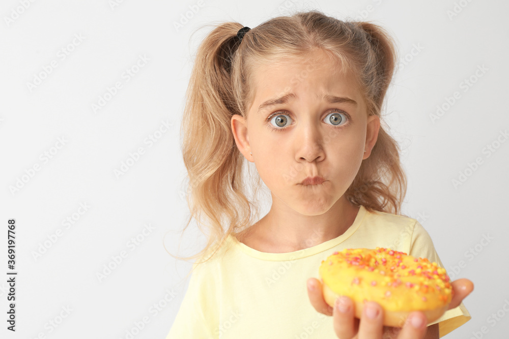 Sad little girl with donut on light background