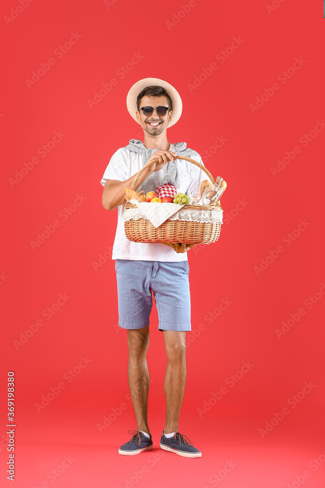 Young man with food for picnic in basket on color background