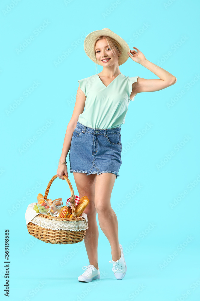 Young woman with food for picnic in basket on color background