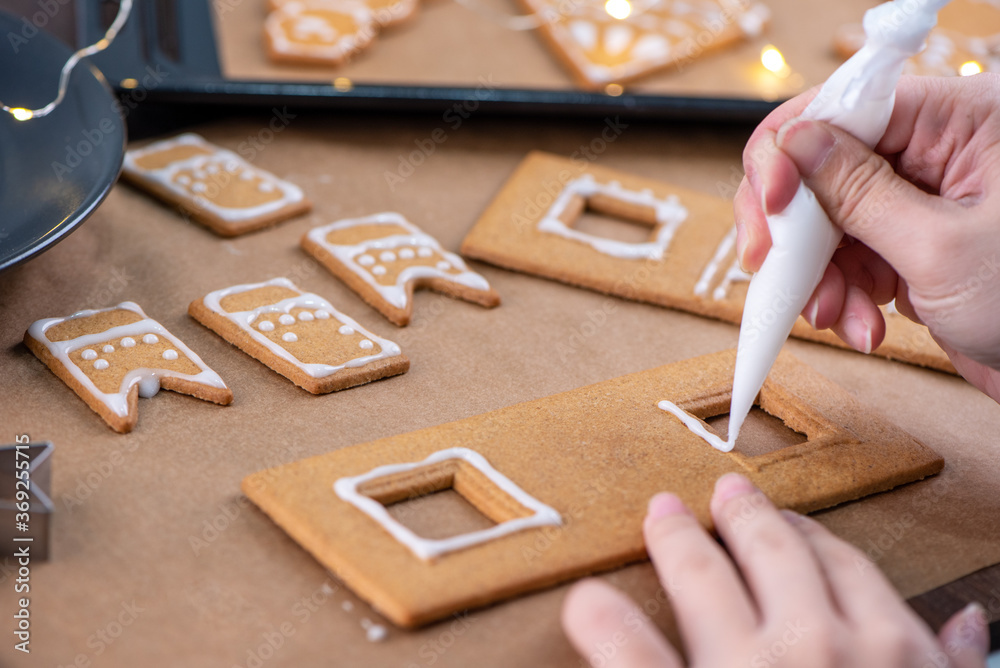 Young woman is decorating Christmas Gingerbread House cookies biscuit at home with frosting topping 