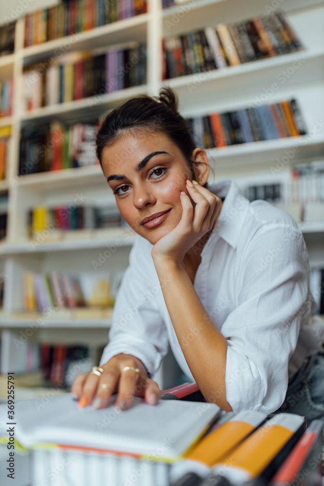 Young girl with brown hair sitting in front of bookshelves.