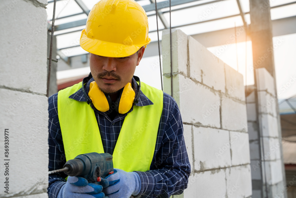 Construction workers using a drilling power tool for drilling aerated bricks on construction site.