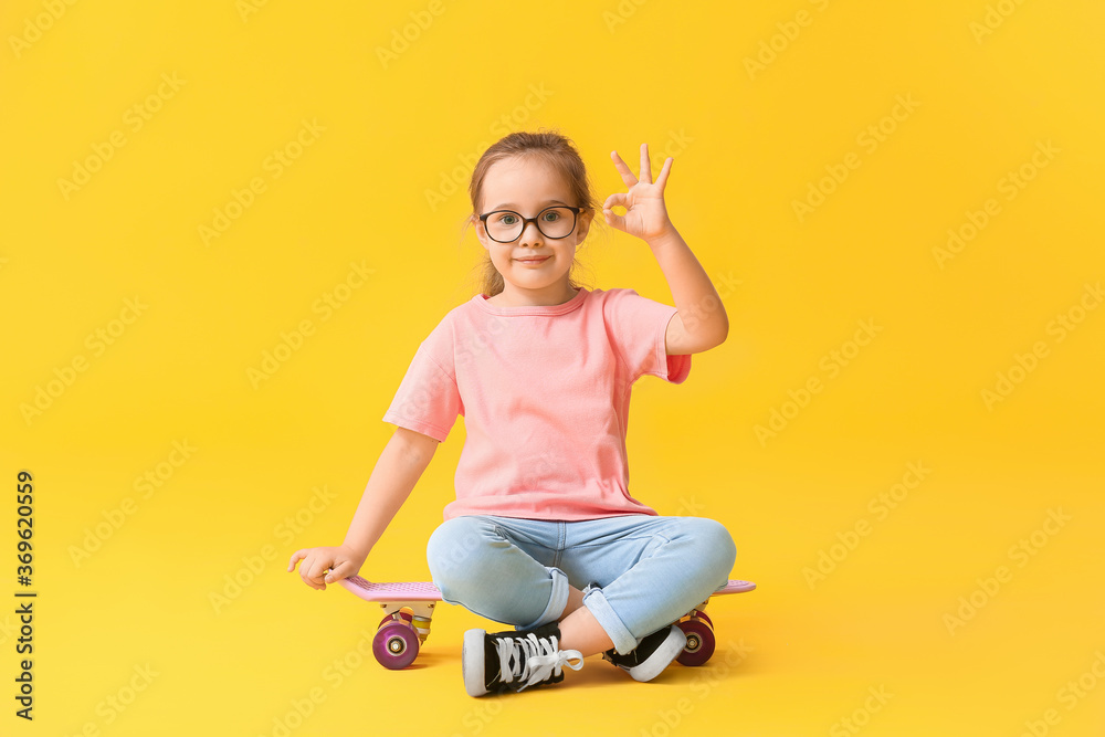 Cute little girl with skateboard showing OK on color background