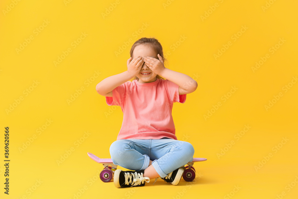 Cute little girl with skateboard on color background