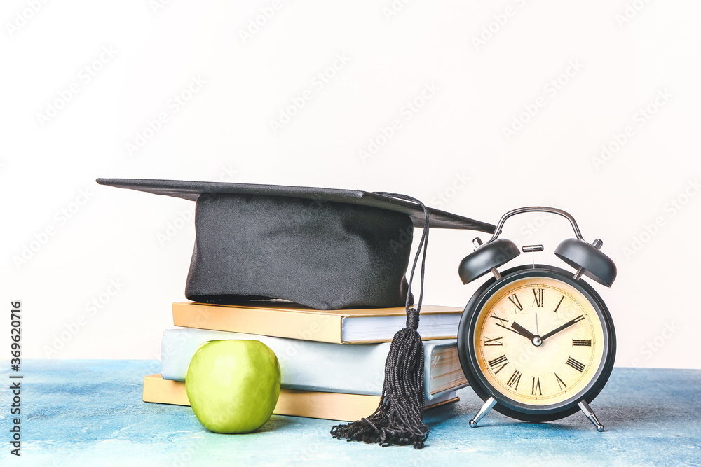 Graduation hat, books, apple and diploma on table against white background