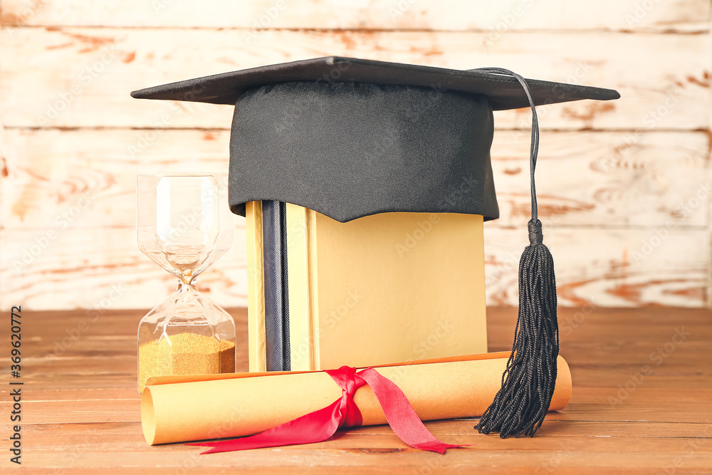 Graduation hat, books, hourglass and diploma on table