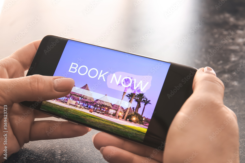 Woman with mobile phone booking room in hotel online, closeup