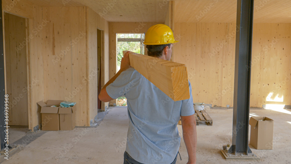 CLOSE UP: Worker carries a log across the first floor of a prefabricated house.