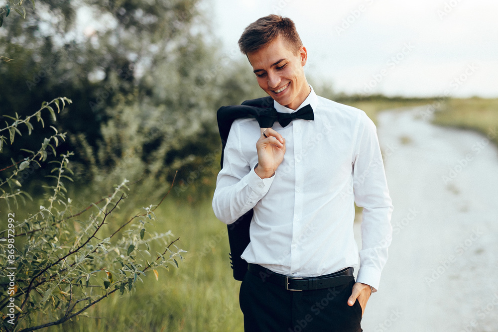 Smiling groom walking on the road wearing his jacket on the shoulder with the green hills on backgro