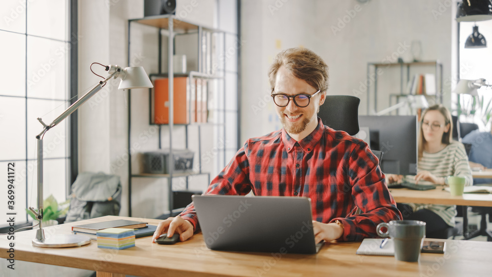 Handsome Smiling Young Man in Glasses and Shirt is Working on a Laptop in a Creative Business Agency