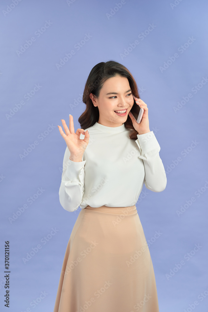 Young woman talking mobile over isolated purple background showing ok sign with fingers