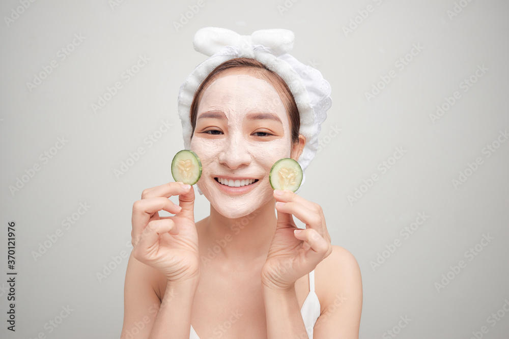 Young woman with clay facial mask holding cucumber slices isolated on white background