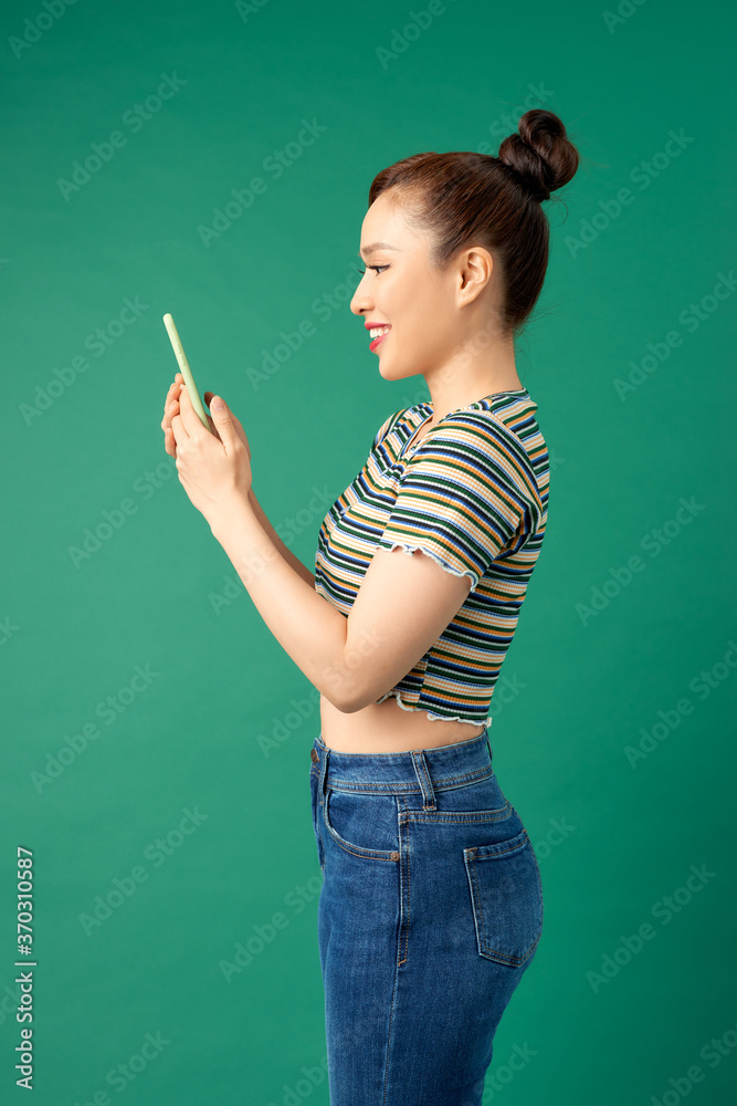 Pretty young Asian woman using smartphone in casual clothign over colorful green background