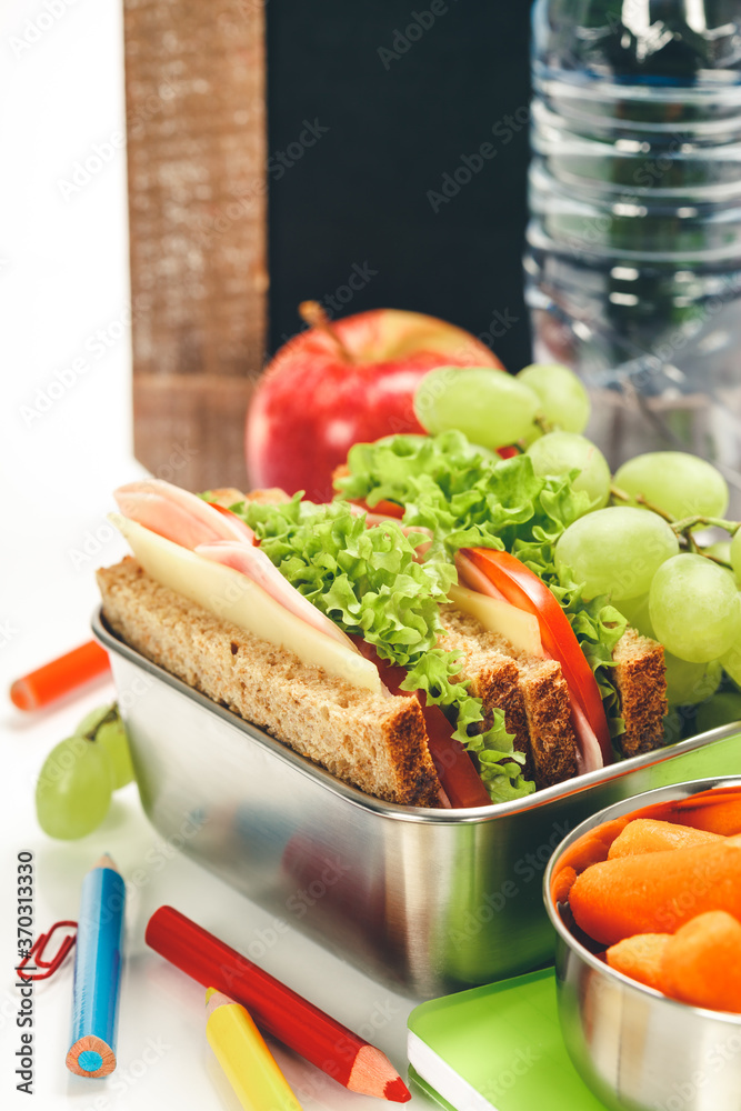 Lunch box with sandwich and fruits infront of chalk board,