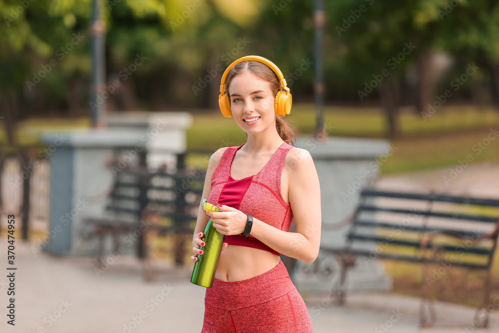 戴着耳机、在户外喝水的运动型年轻女性