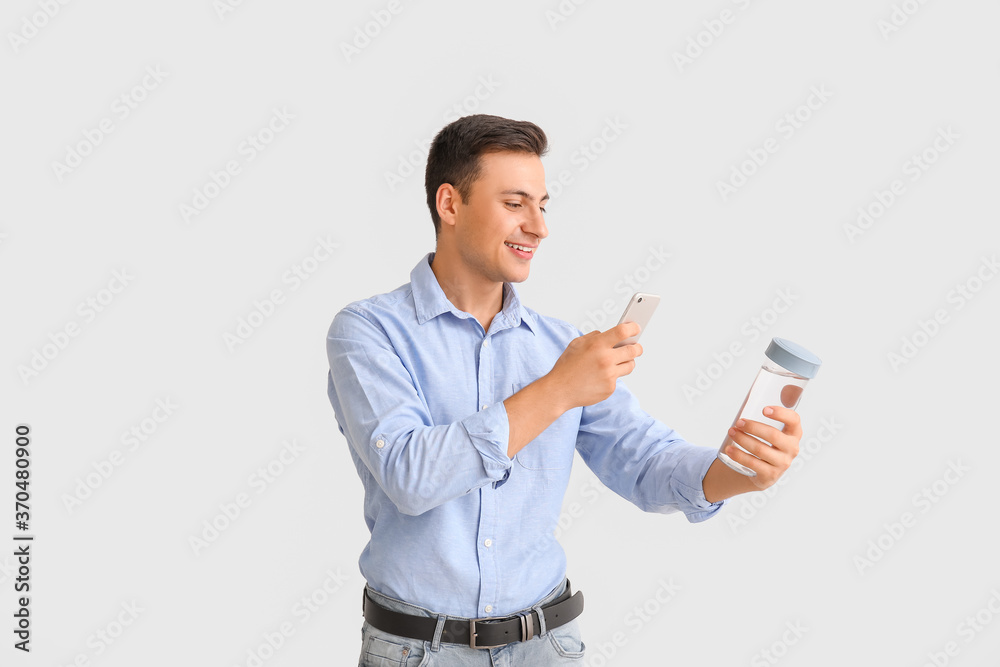 Young man with bottle of water and phone on light background