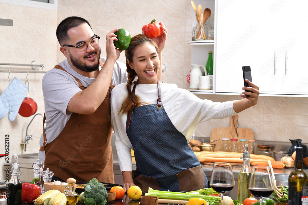 Loving young Asian couple cooking in kitchen making healthy food together feeling fun and using smar