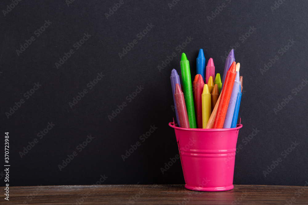 colored crayons on the wooden table, blackboard background