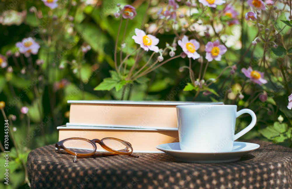 A cup of coffee, a glasses and the  book on the brown table with morning light and blurred nature ba