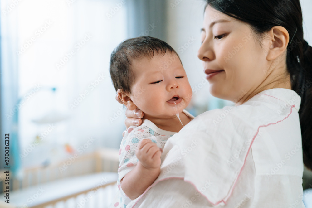 特写日本母亲肩上裹着布，正在给孩子打嗝。亚洲可爱的婴儿被她的妈妈抱着