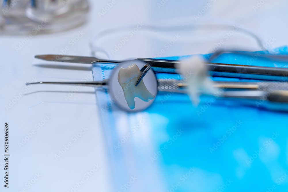 Metal dentist instruments over medical mask. White table background. Selective focus.