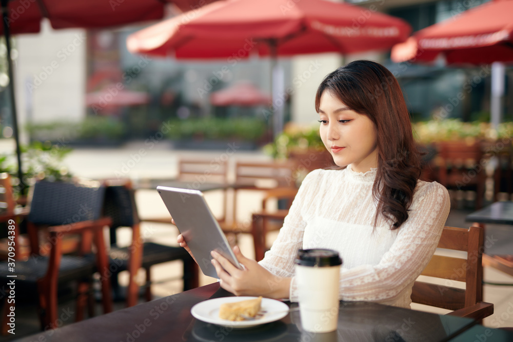 Young and beautiful Asian woman using her tablet PC while sitting at outdoor coffee shop in the urba