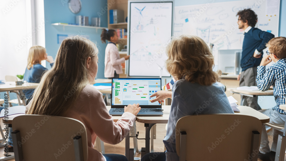 Elementary School Science Class: Over the Shoulder Little Boy and Girl Use Laptop with Screen Showin