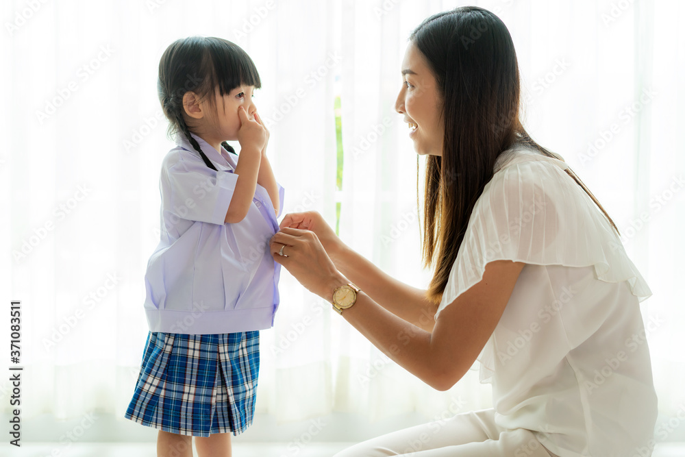 Asian mother preparing kindergarten student uniform to her little daughter for school getting ready 