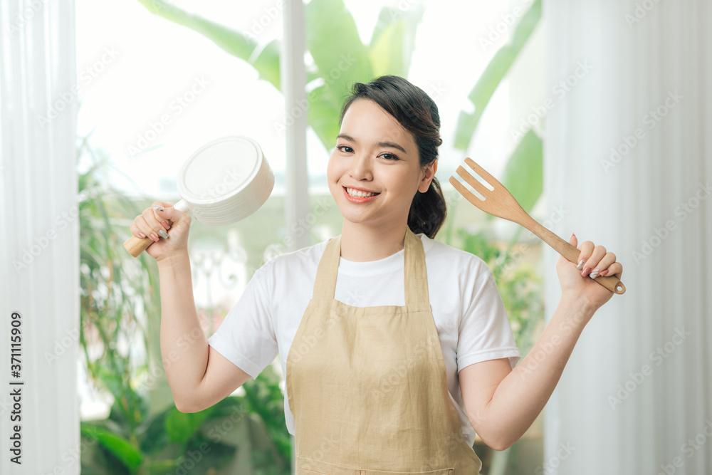 在大窗户附近的手煎锅和厨房抹刀里穿着围裙的女人