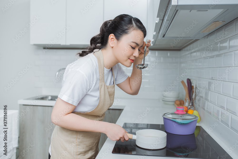 年轻女人在厨房用勺子品尝食物