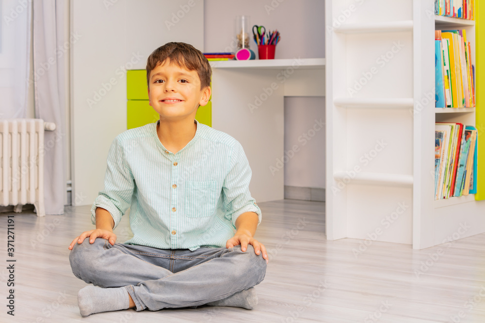 Smiling calm little boy sit in his room with positive expression