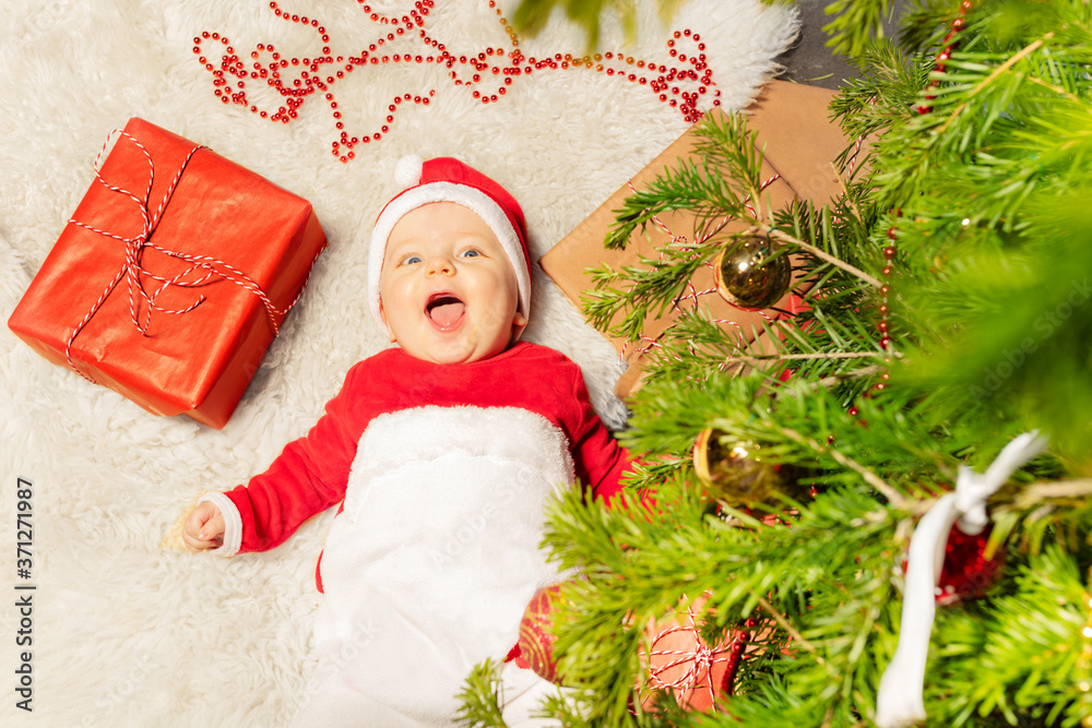 Happy little toddler boy lay on the carpet with open mouth laughing and looking at camera under Chri