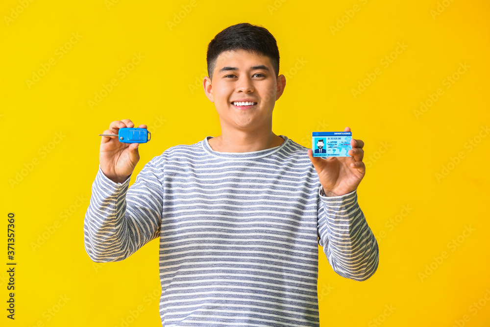 Happy Asian man with car key and driving license on color background