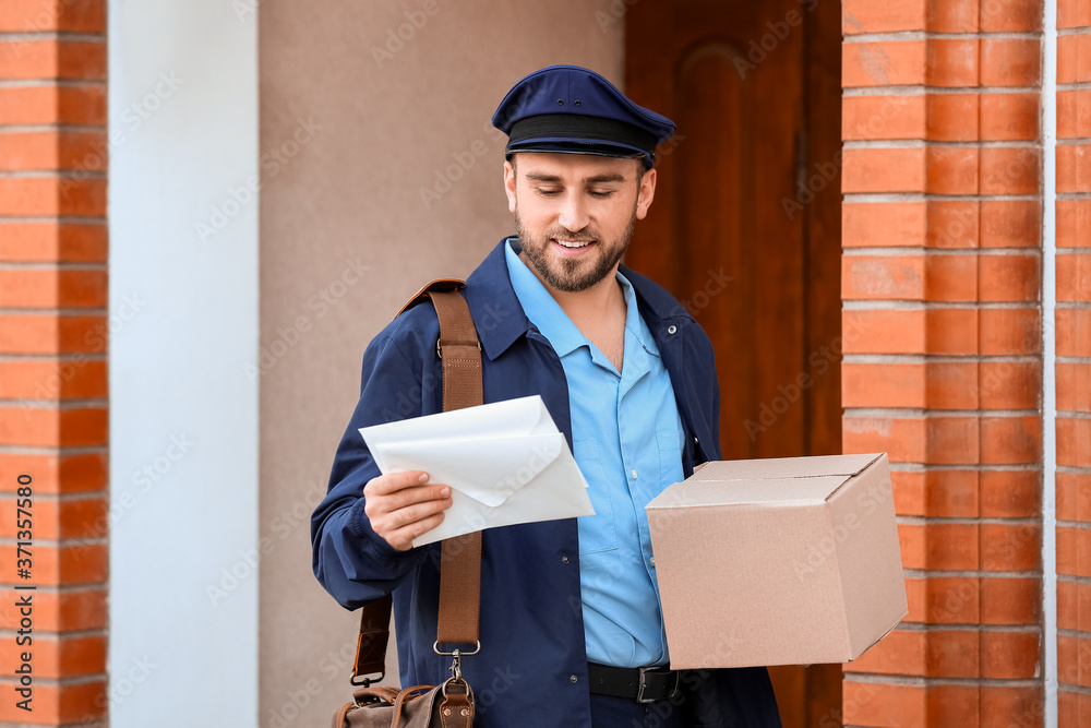 Handsome young postman with parcel and letters outdoors