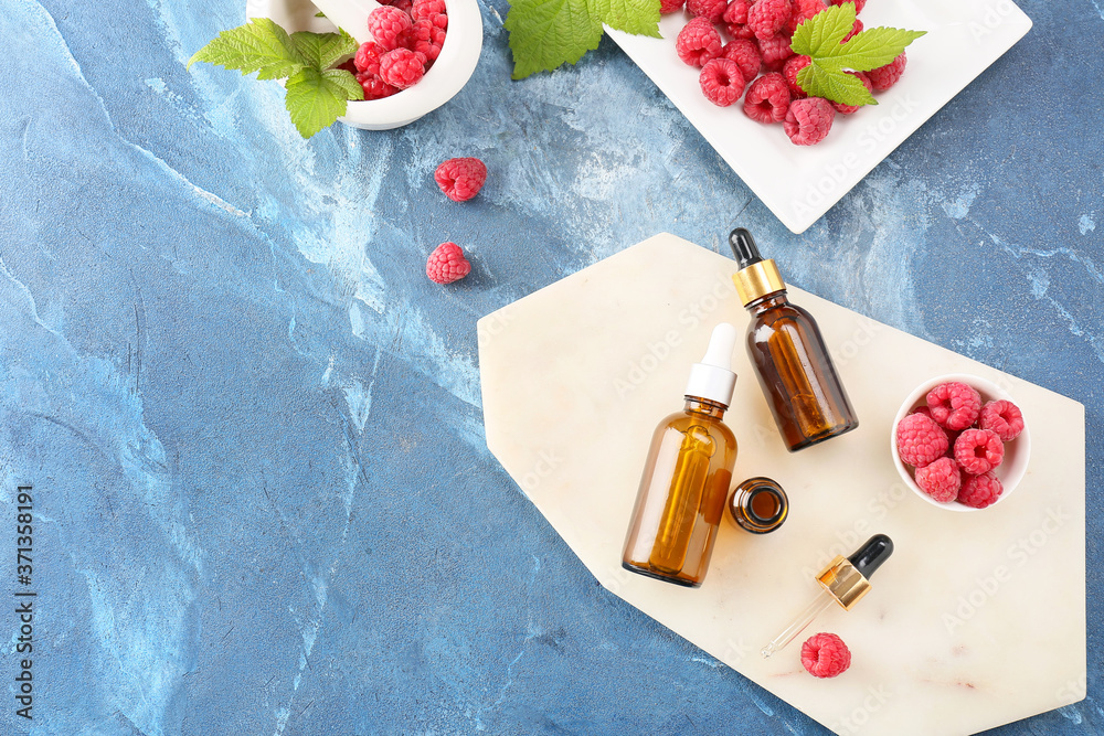 Bottles of raspberry essential oil on color background