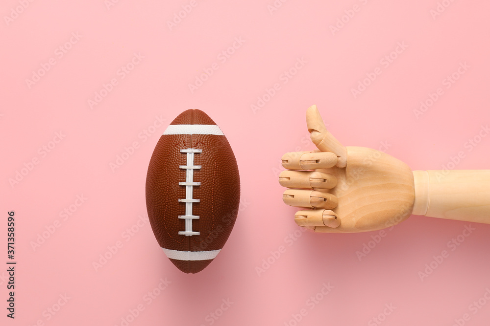 Hand of mannequin with rugby ball on color background