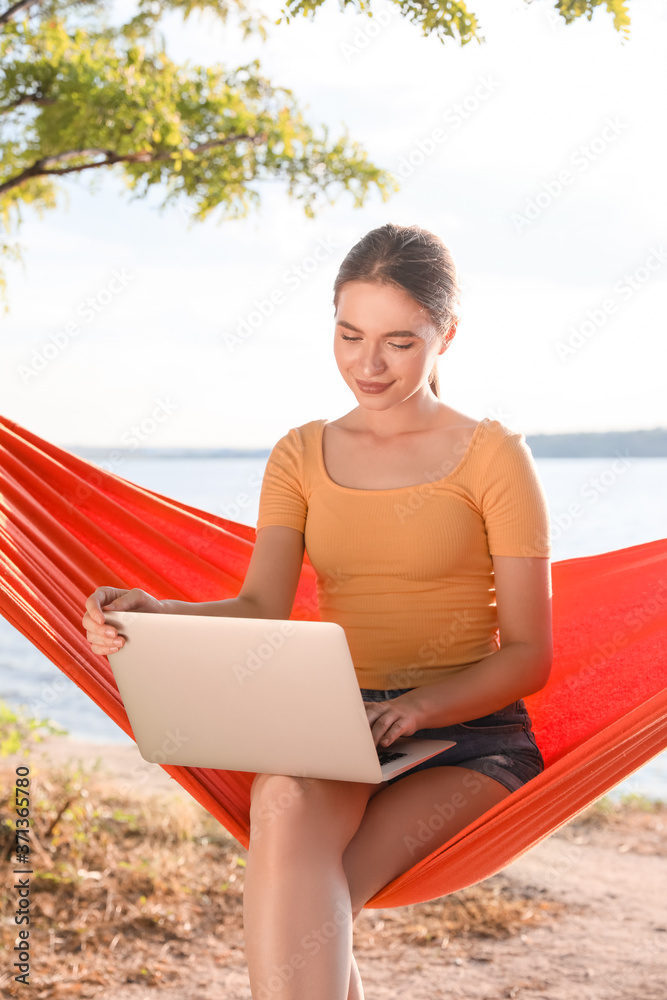 Young woman with laptop relaxing in hammock outdoors