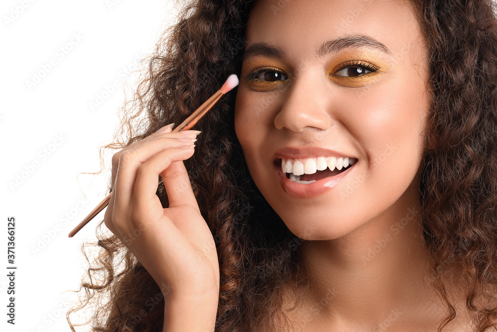 Beautiful young African-American woman with makeup brush on white background