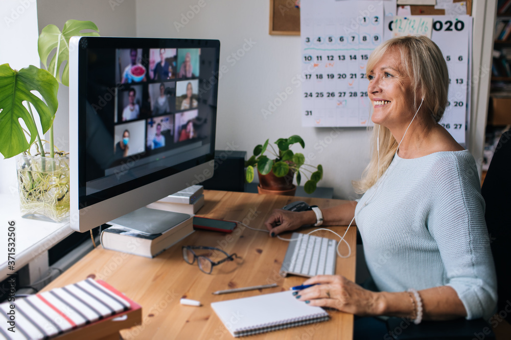 Smiling mature woman having video call via computer in the home office. Online team meeting video co