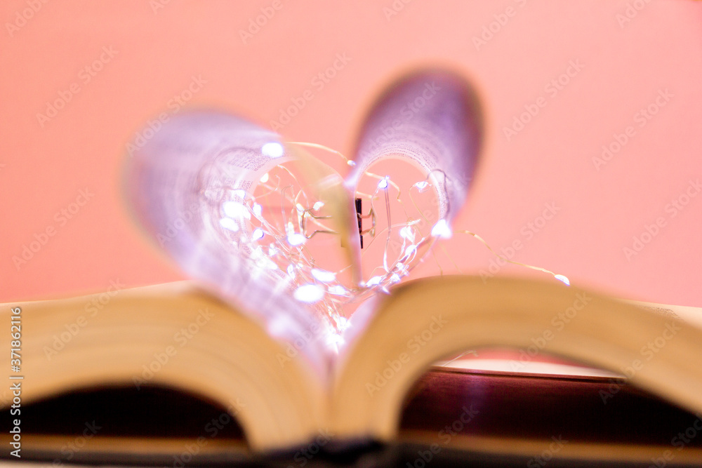 Open book with heart shaped sheets decorated with bright garlands of lights and highlights in the ba