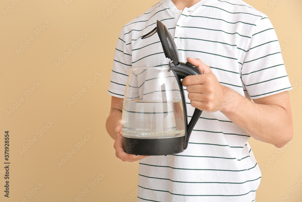 Young man with electric kettle on color background