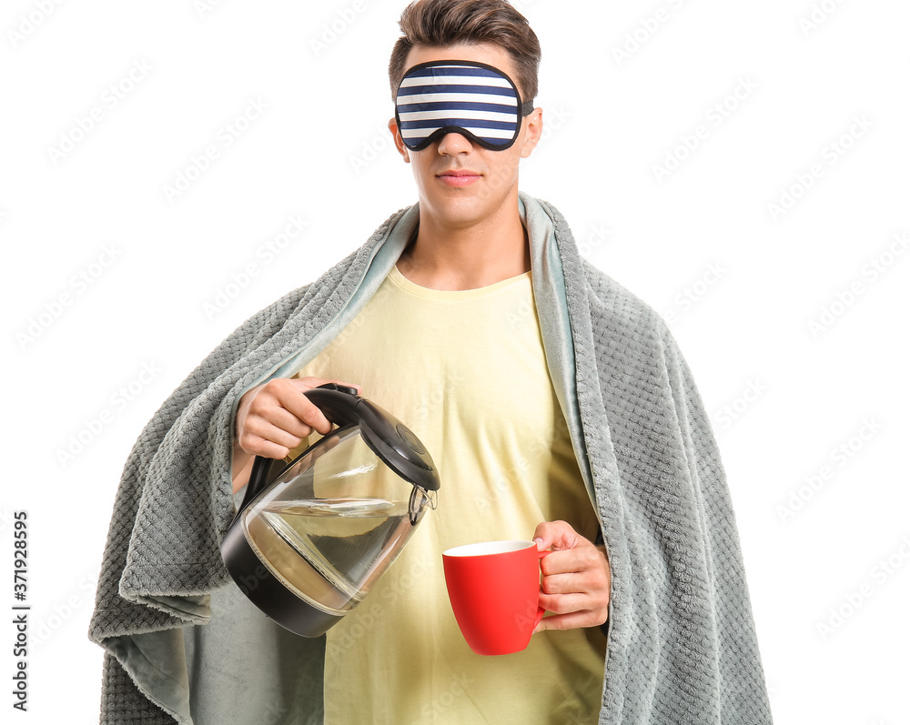 Sleepy young man pouring water from electric kettle in cup on white background