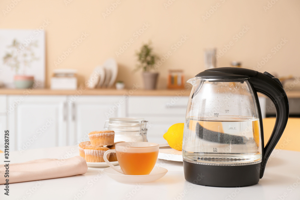 Electric kettle, cup of tea and pastry on kitchen table